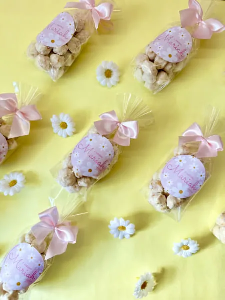 Saquinhos de pipoca gourmet com laço rosa e margaridas sobre fundo amarelo